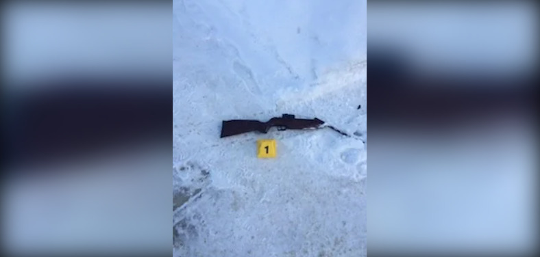 A photo of a rifle-style gun lying in the snow with a yellow crime scene card labelled "1" next to it.