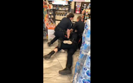 A screengrab from the bystander video of the incident, showing three police officers piled on top of another person sprawled on the floor of a convenience store.