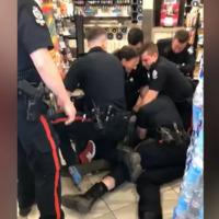 A screengrab from the bystander video of the incident, showing six police officers pinning a person to the floor, with another officer standing in the foreground