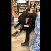 A screengrab from the bystander video of the incident, showing three police officers piled on top of another person sprawled on the floor of a convenience store.